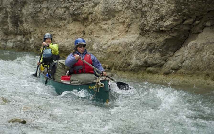 two people paddle a canoe through whitewater on an outward bound gap year course
